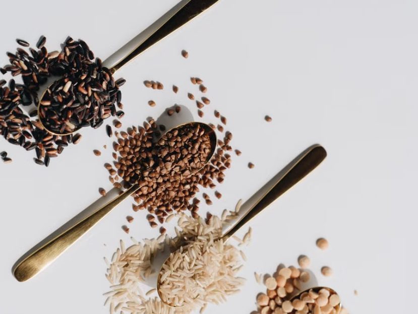 Top view of various dry grains on spoons against a white background, showcasing a variety of textures and colors.